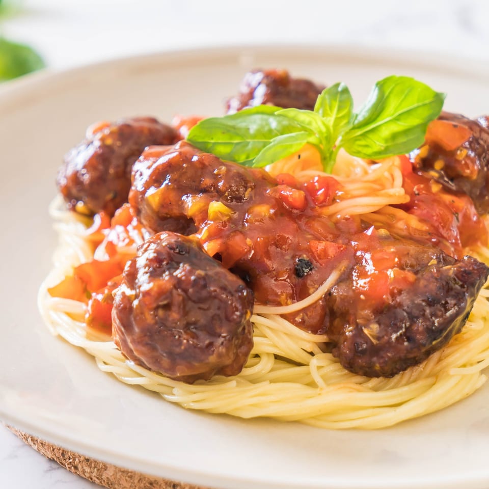 Spaghetti and meatballs with tomato sauce and fresh basil on a white plate.