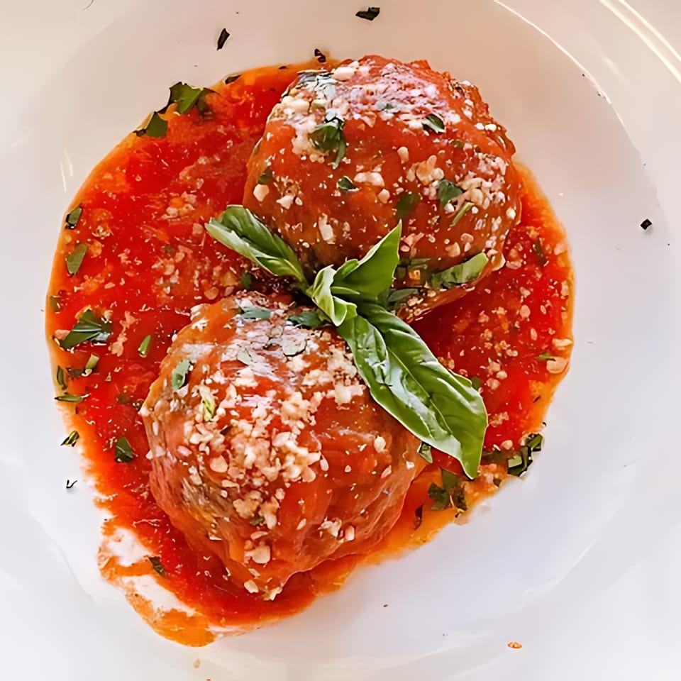 Two large meatballs in red sauce, topped with cheese and basil, on a white plate.