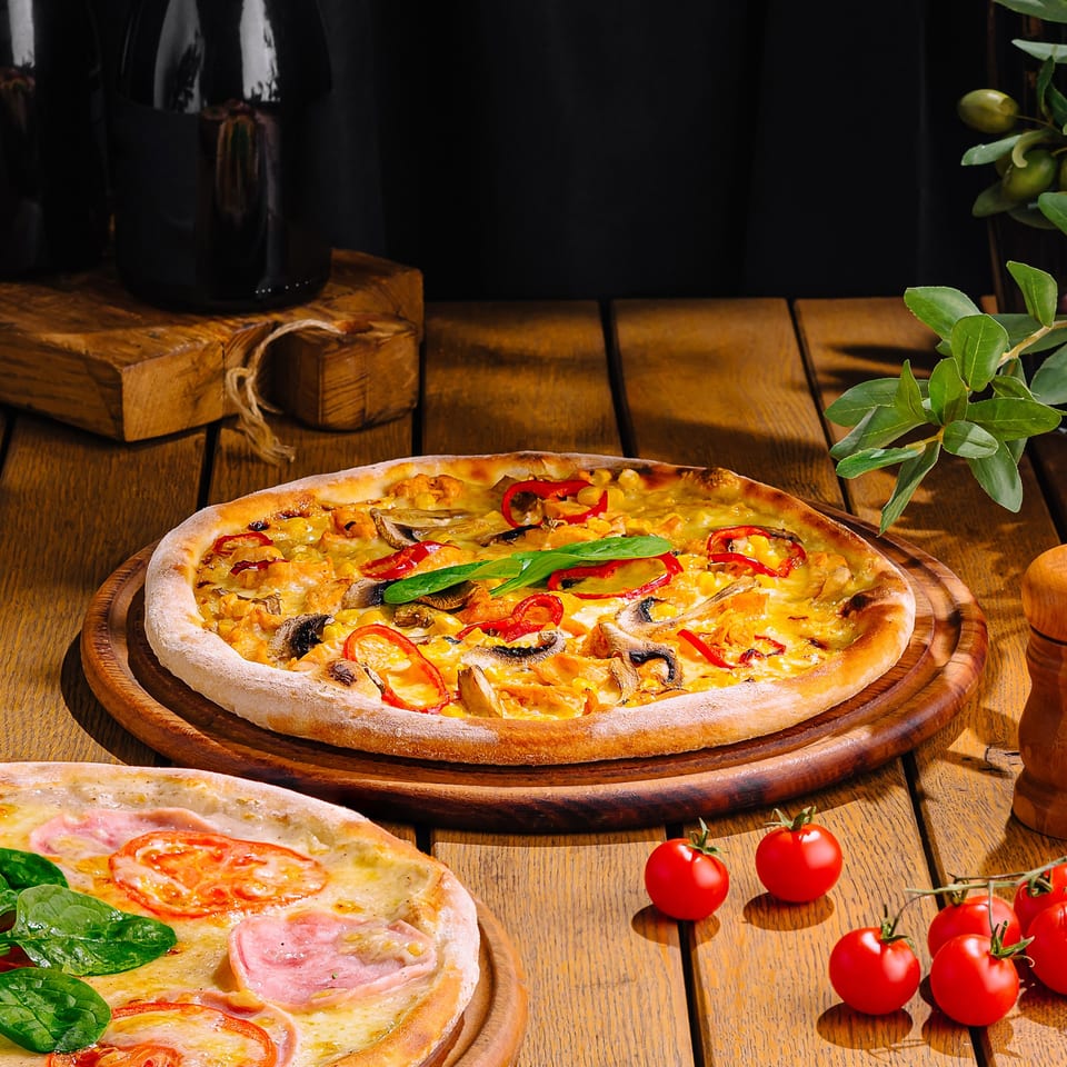 Two Soho Pizza & Grill pizzas on wooden boards, one with mushrooms and peppers, the other with ham and tomatoes.